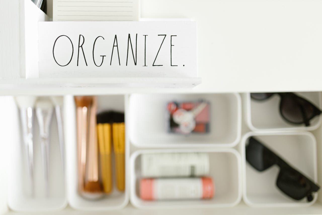 Stylish arrangement of makeup brushes, sunglasses, and accessories in white compartments with Organize label.