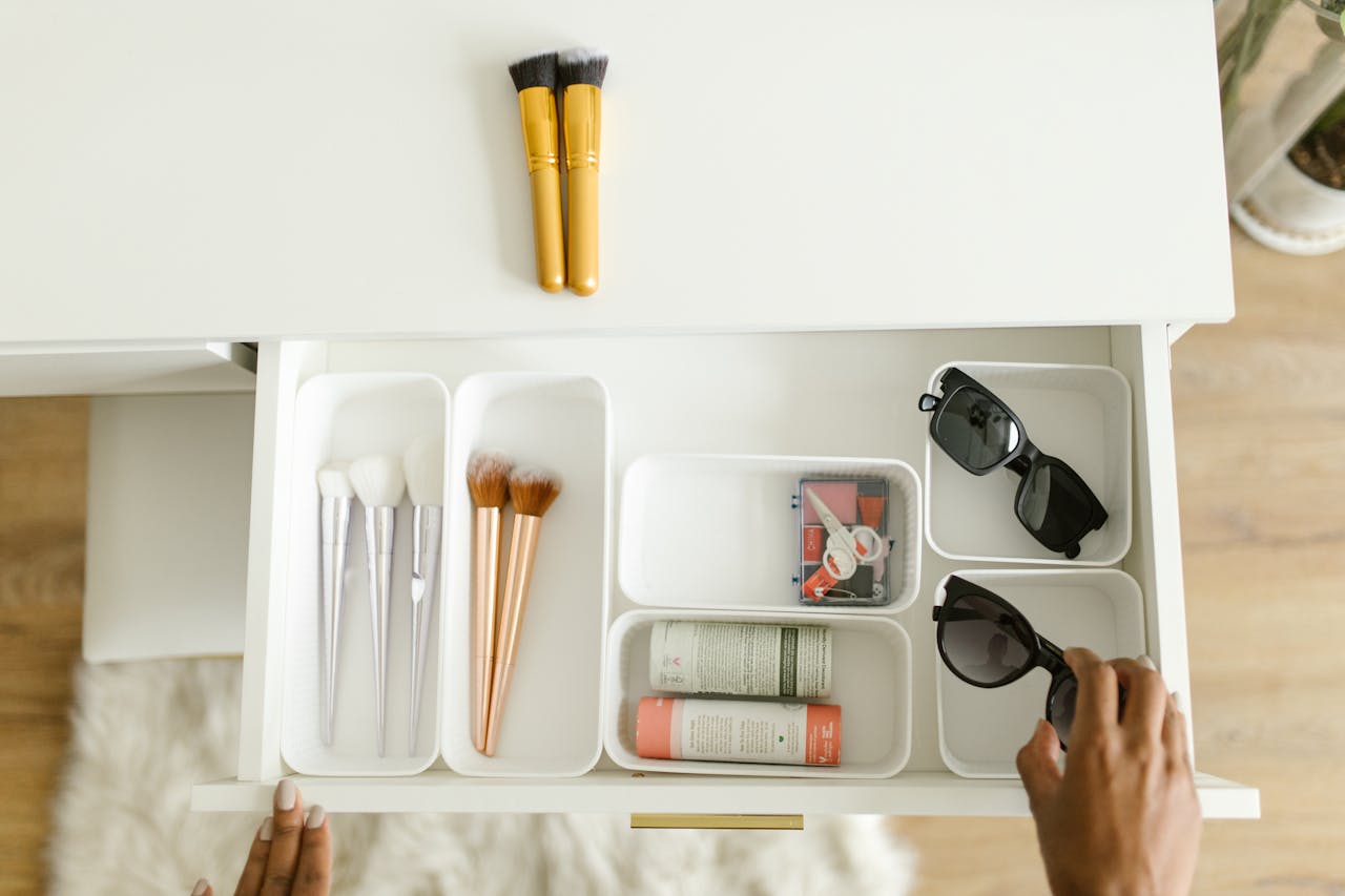 A top-view photo of an organized drawer containing sunglasses, makeup brushes, and skincare items.
